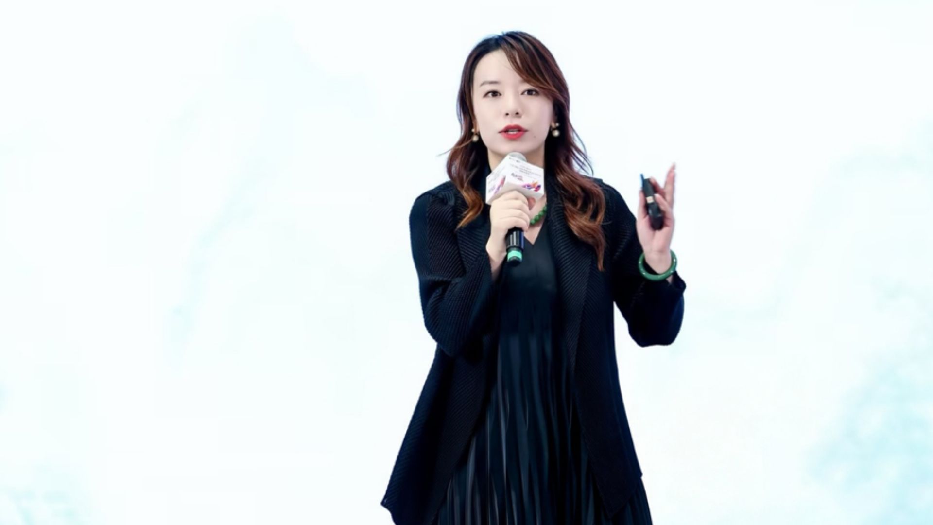 一名身穿黑衣的女子手持演示遥控器，对着麦克风讲话。